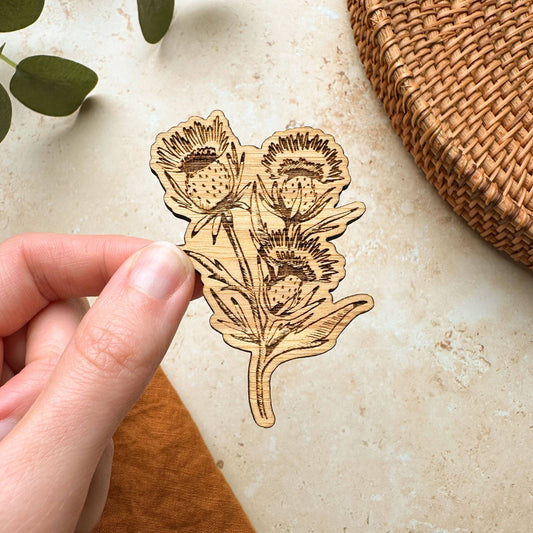 A hand holding a wooden magnet shaped like a thistle flower