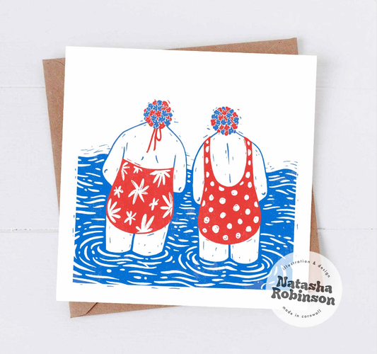 A square greetings card featuring a linocut illustration of two stylized ladies standing in water, wearing red and blue swimsuits with a floral pattern. 