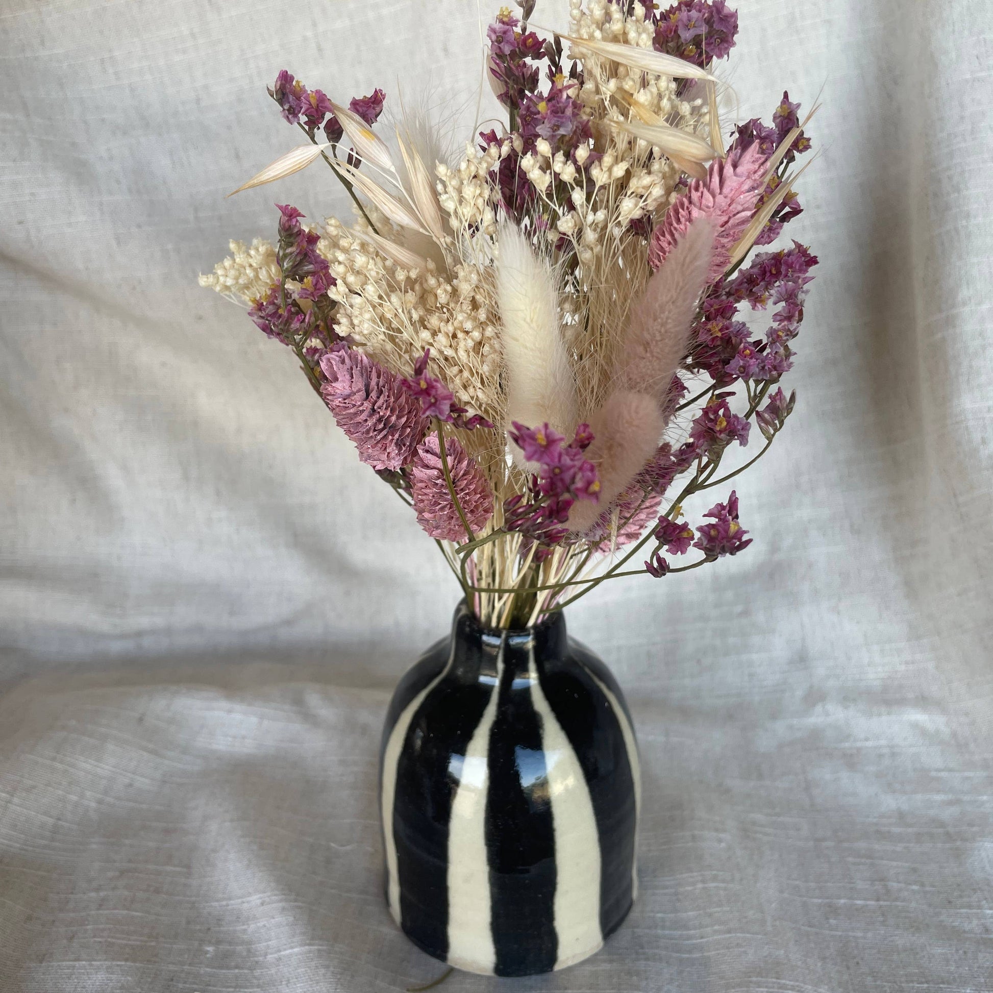 Black and white striped vase with dried flowers on a beige fabric background