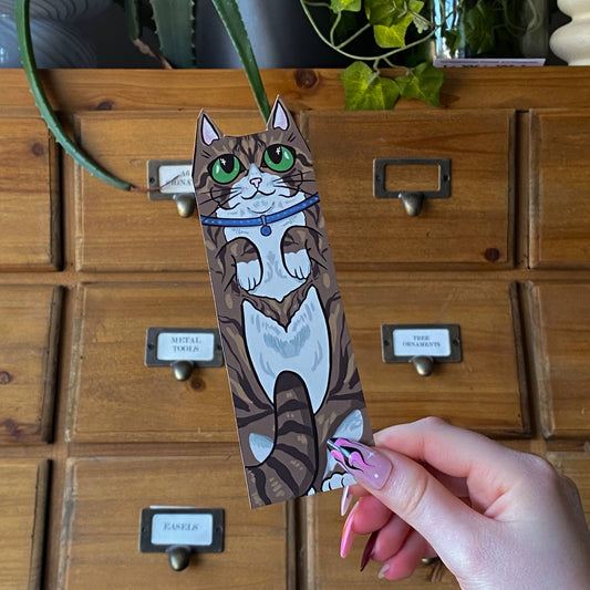 Hand holding a cat-shaped bookmark in front of a wooden drawer