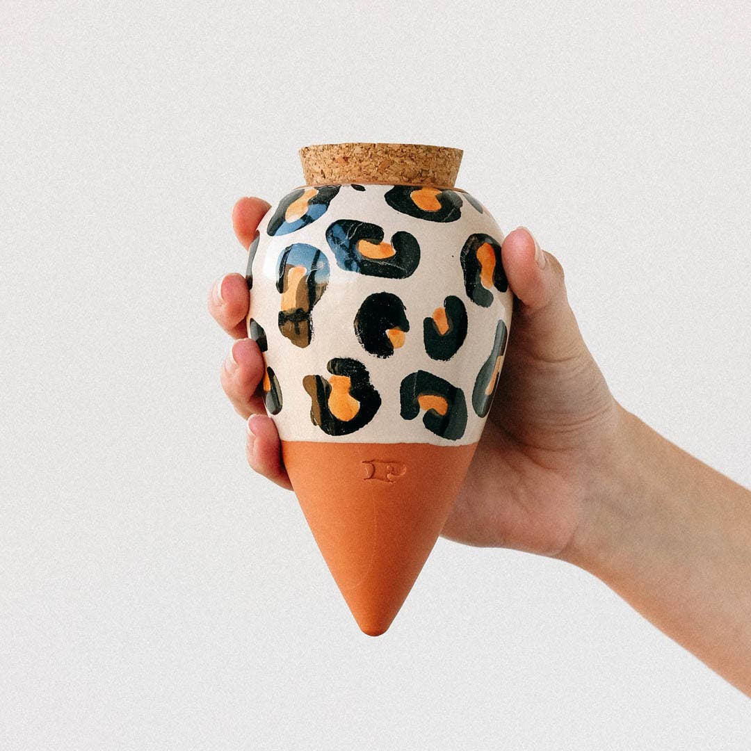 A hand holding a conical terracotta watering spike with a leopard print design, almost fully filled with water.