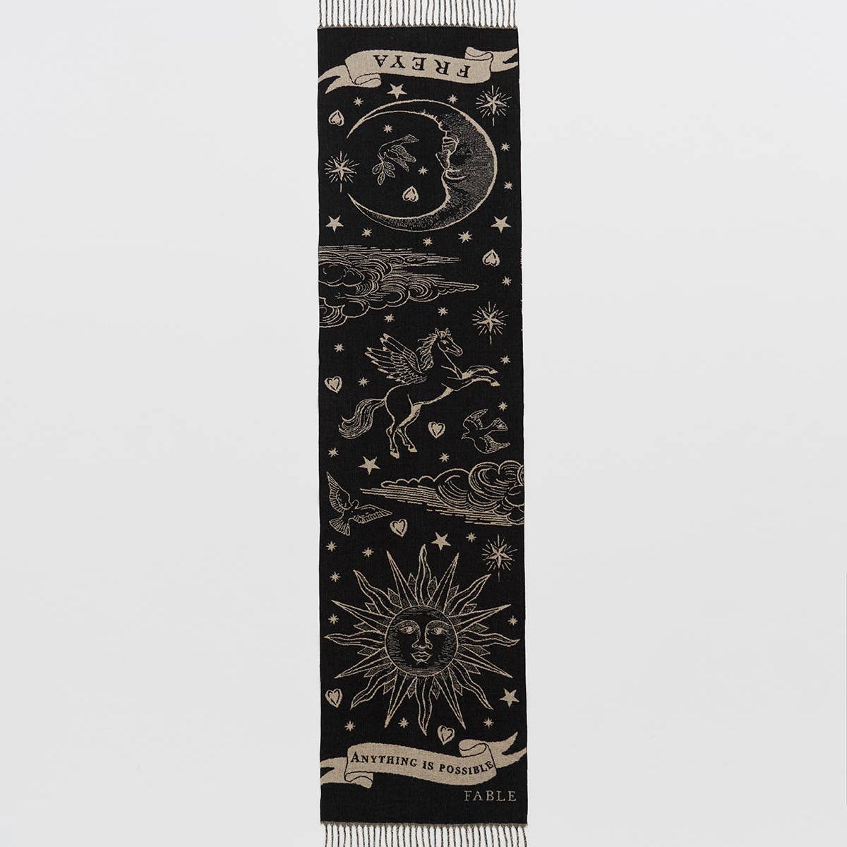 A long black scarf with fringe ends, featuring celestial and mythological motifs including a crescent moon, sun, stars, and a winged horse in an off white colour.