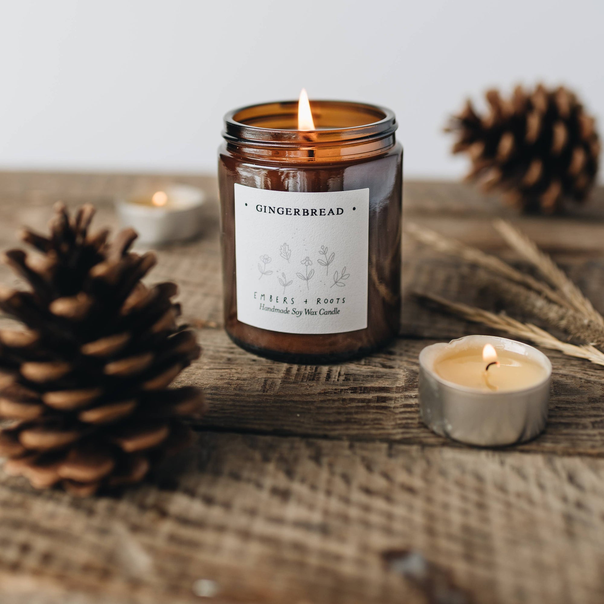 Gingerbread scented candle in a glass jar with pinecones and a small candle on a wooden surface.