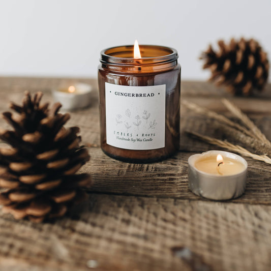 Gingerbread scented candle in a glass jar with pinecones and a small candle on a wooden surface.