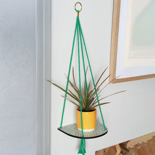 Green macrame plant hanger with a yellow pot and plant against a white wall.