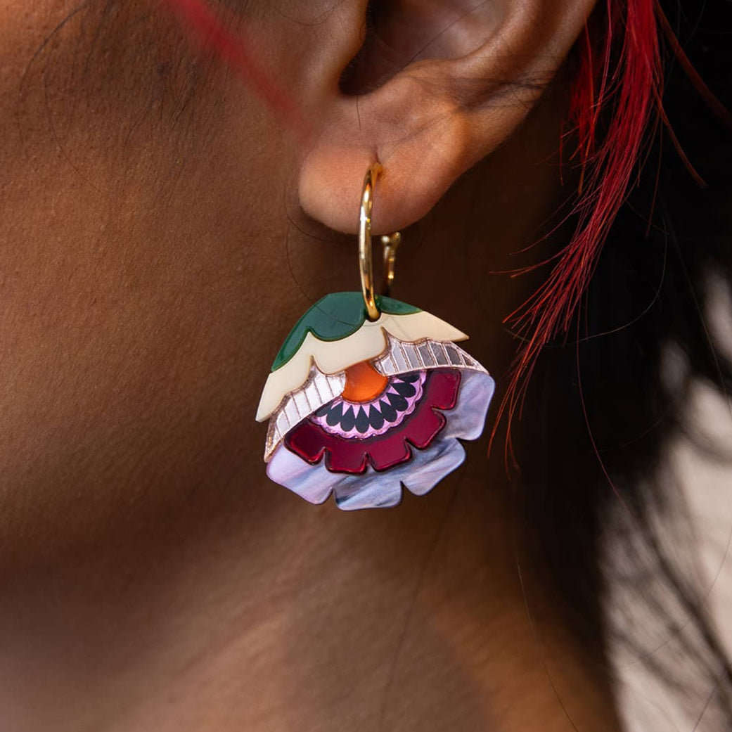 Close-up of a person wearing a colorful floral earring with red hair.