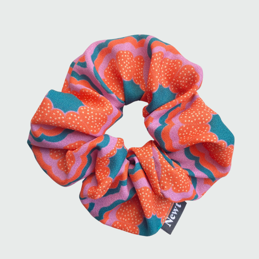 Colorful patterned scrunchie with a Newt brand tag on a light gray background