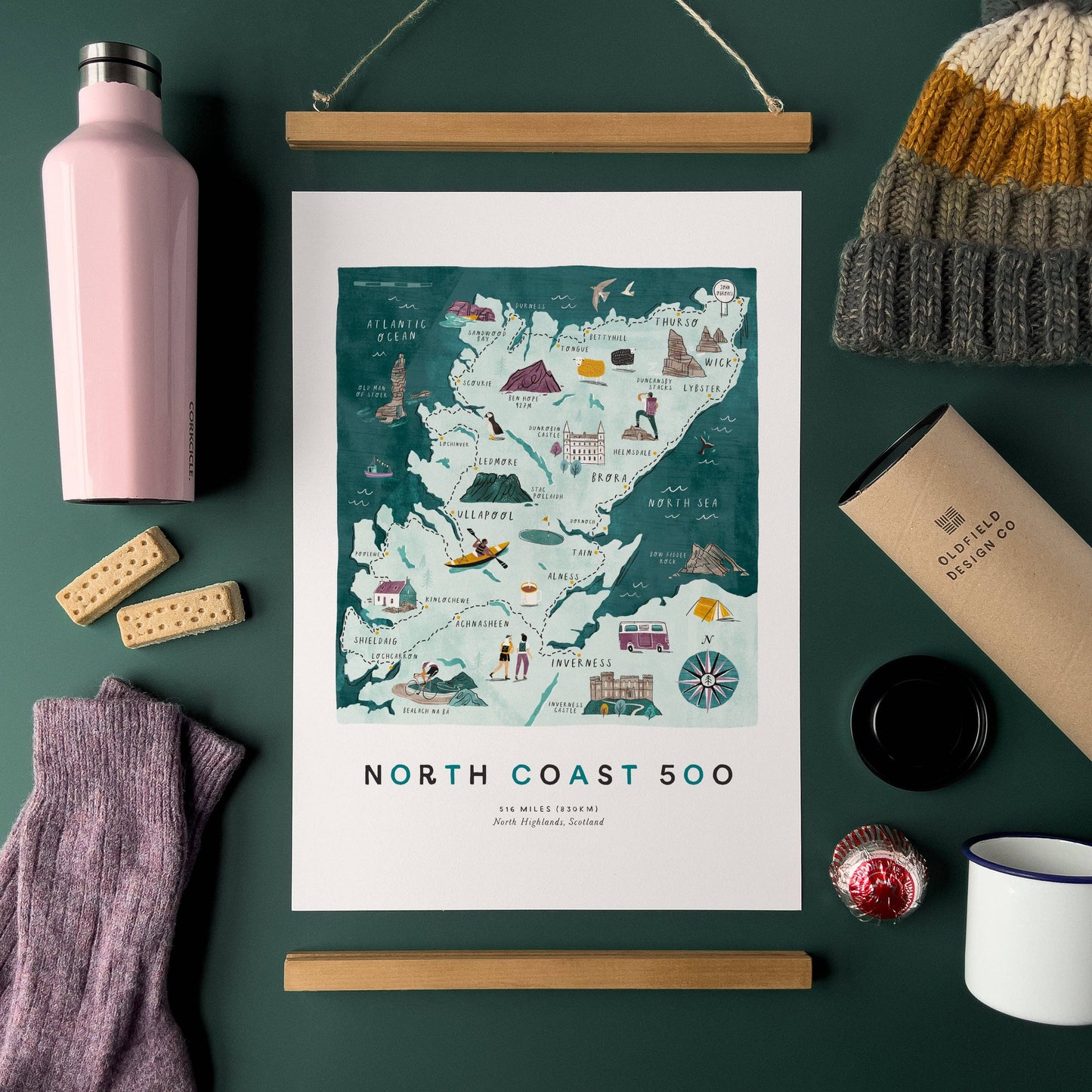 Map of North Coast 500 with a pink water bottle, beanie, and other items on a dark green background
