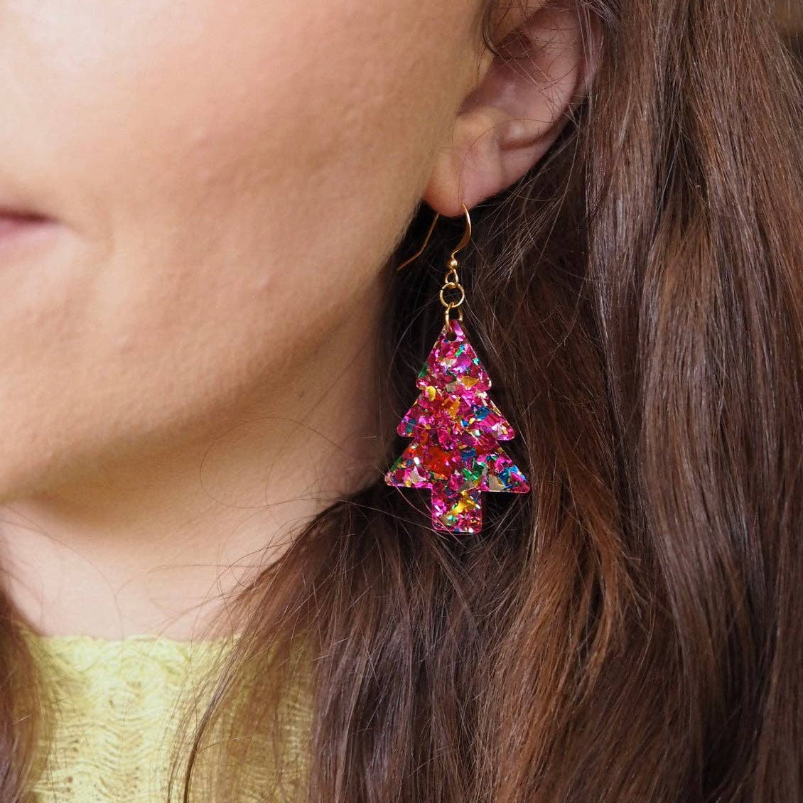 Close-up of a person wearing colorful tree-shaped earrings with a gold top.
