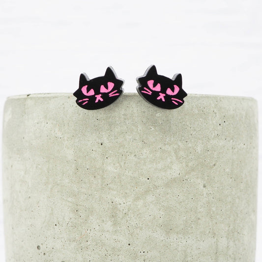 Black cat-shaped earrings with pink accents on a textured surface