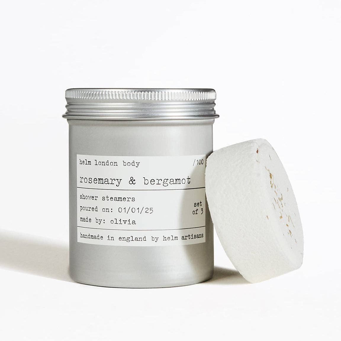 Shower steamer with a metallic tin labeled 'rosemary & bergamot' on a white background