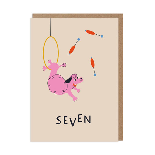 A greeting card featuring an illustration of a pink juggling circus poodle with the number 7 on it, along with a brown kraft envelope.