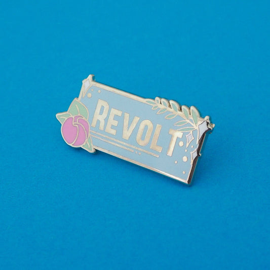 A powder blue enamel pin with the word 'REVOLT' written on it