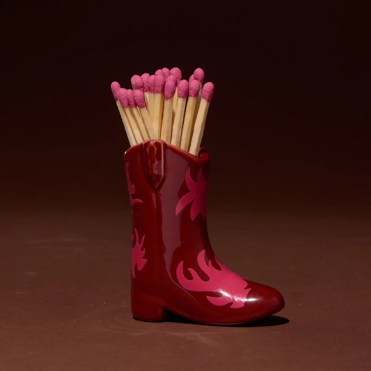 Retro style cowboy boot match holder in red and pink sitting on a dark background