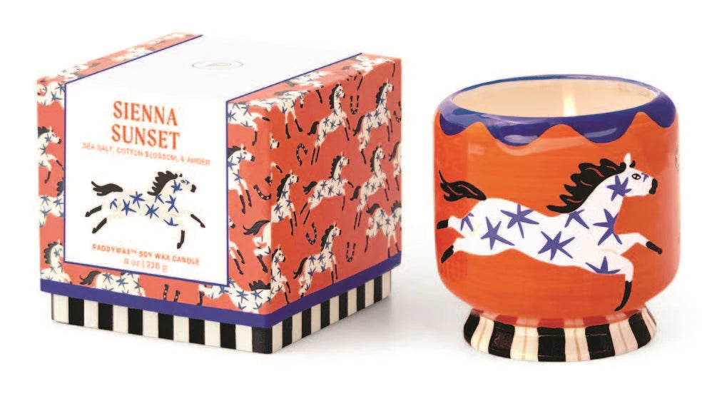 candle in a decorative ceramic holder with a horse painted on the side. It sits next to a decorative printed box.