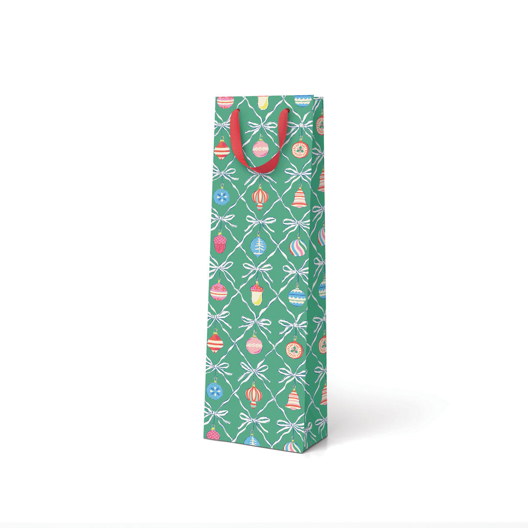 A bottle sized gift bag in green with vintage style decorations illustrated on it, with a red ribbon handle
