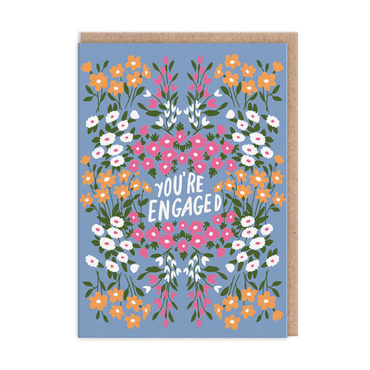 A greeting card with a floral design and the text 'YOU'RE ENGAGED' in the center. The card is accompanied by a Kraft envelope.