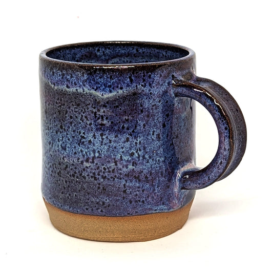 A handcrafted ceramic mug with a purple and blue sunset color palette and a matte finish on the lower half, transitioning to a glossy finish on the upper half.