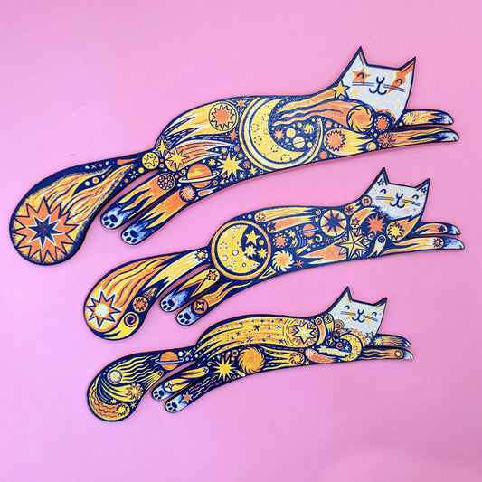 A set of three colorful wooden cat shapes with intricate patterns and designs, displayed against a pink background.