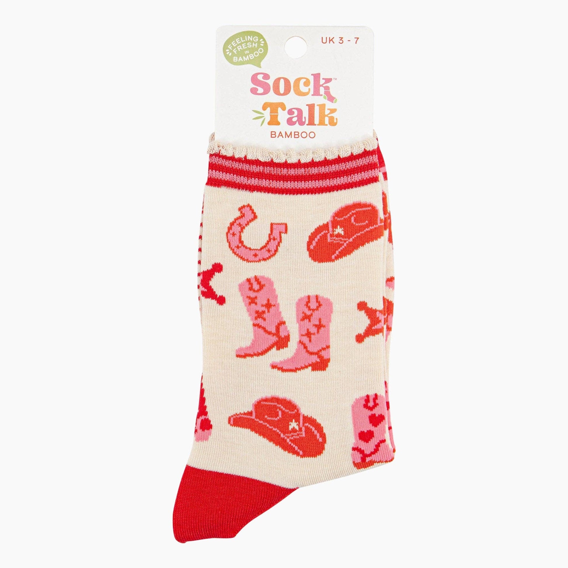 A pair of ankle socks with a western cowgirl theme, featuring red boots and accessories on a cream background with red stripes at the heel. Shown in it's packaging.