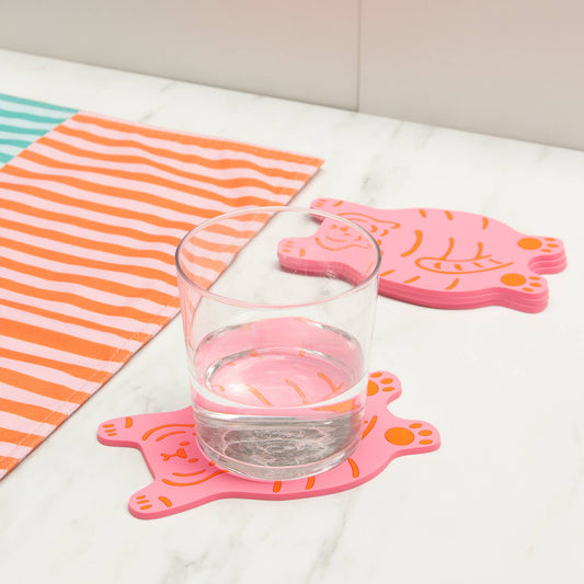 Glass of water on pink tiger-shaped coasters with a striped towel in the background