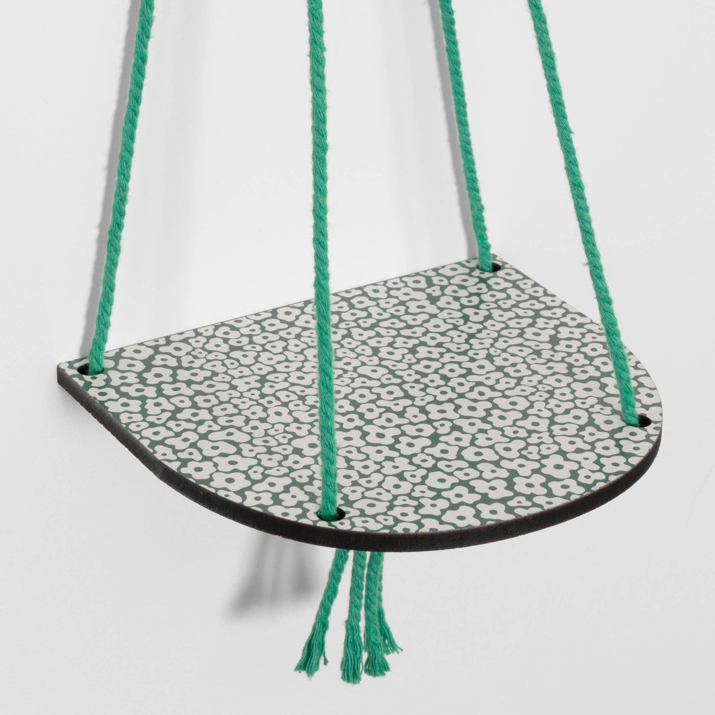 Hanging shelf with a patterned base and green cords on a white background