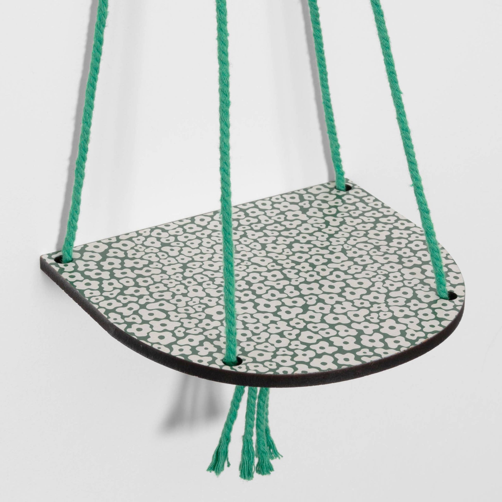 Hanging shelf with a patterned base and green cords on a white background