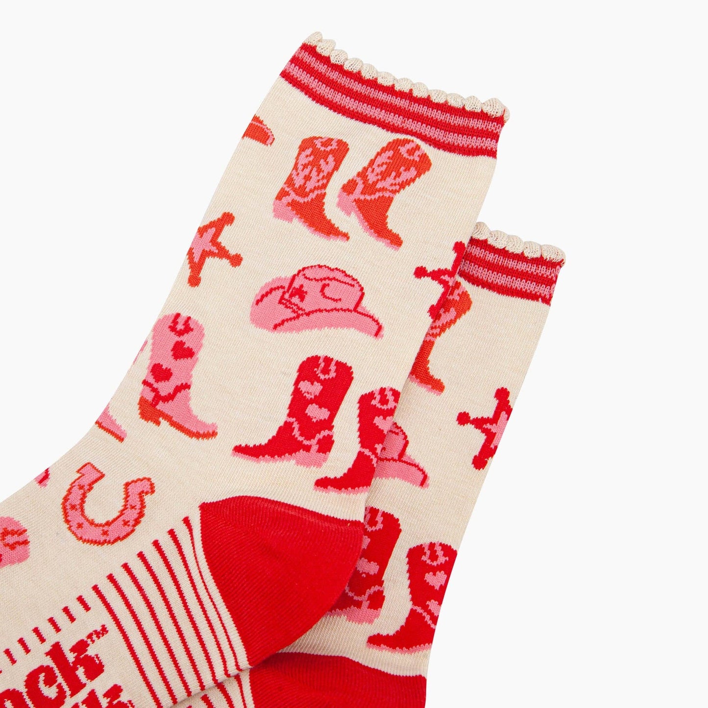 A pair of ankle socks with a western cowgirl theme, featuring red boots and accessories on a cream background with red stripes at the heel. Close up of ribbed cuff detail.