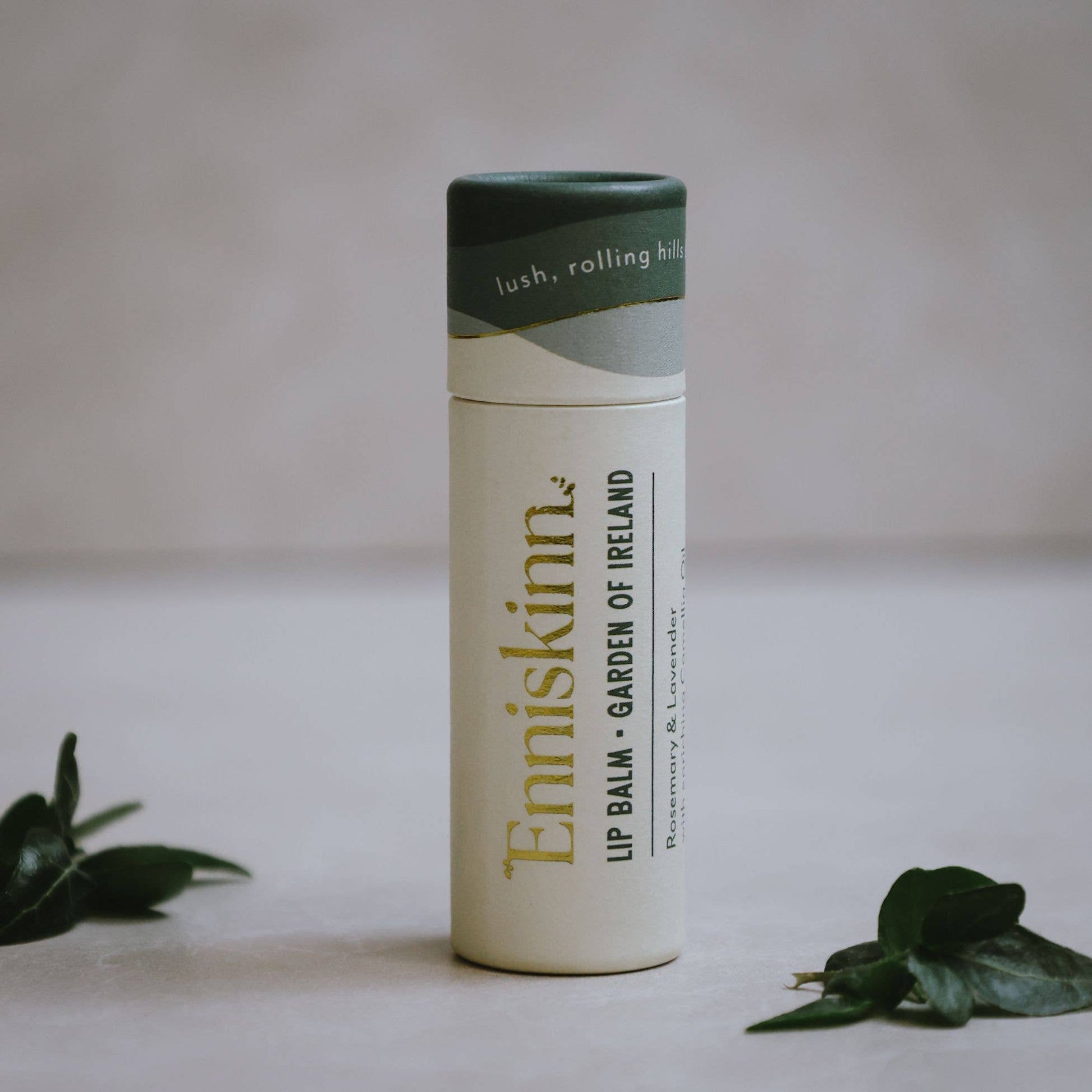 Enriskinn lip balm container on a neutral background with green leaves.