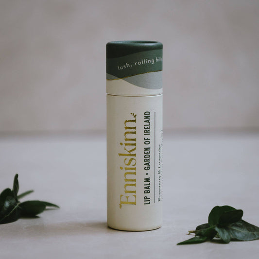 Enriskinn lip balm container on a neutral background with green leaves.
