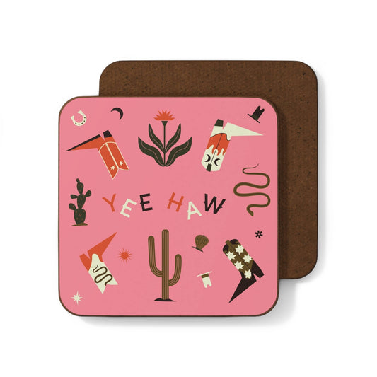 A 'Yeehaw' themed square coaster with a pink background, featuring western-inspired illustrations such as a boot, cactus, and text. The coaster lies on a contrasting brown surface.