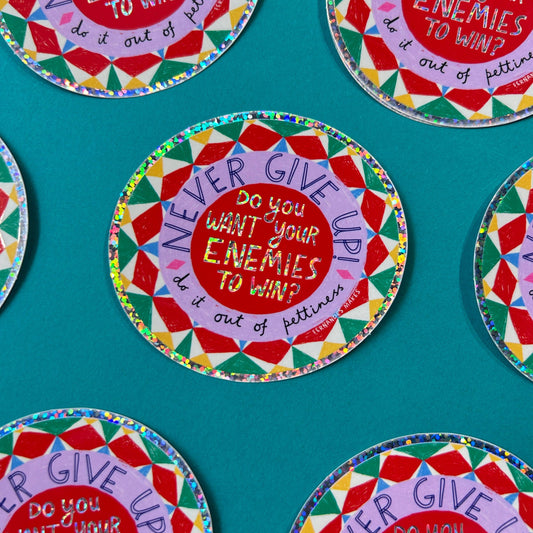 Several colorful round stickers are arranged on a teal background. Each card has a red center with the phrase “Do you want your enemies to win?” in white text, surrounded by a multicolored geometric pattern and a purple ring reading “Never give up, do it out of pettiness"