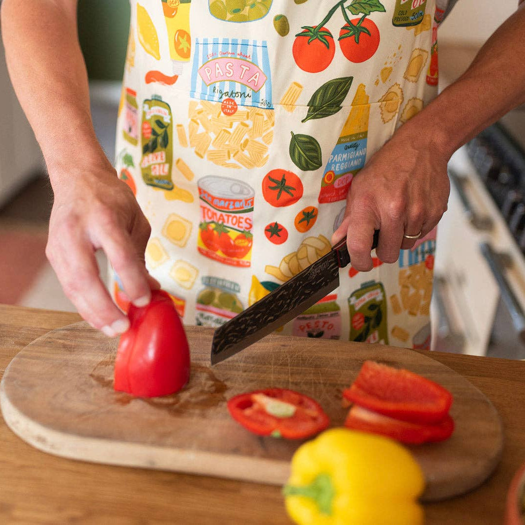 Person cutting peppers wearing an apron with hand drawn illustrations of Italian food ingredients