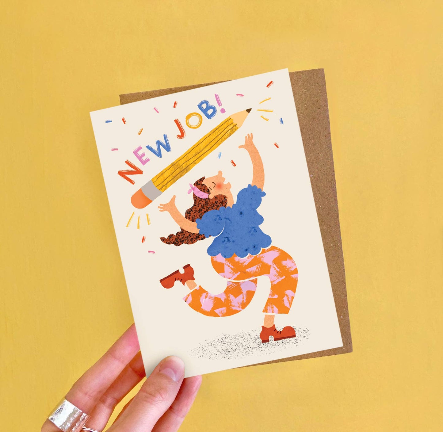 Greeting card with illustration of a person holding a large pencil and 'NEW JOB!' text on a yellow background.