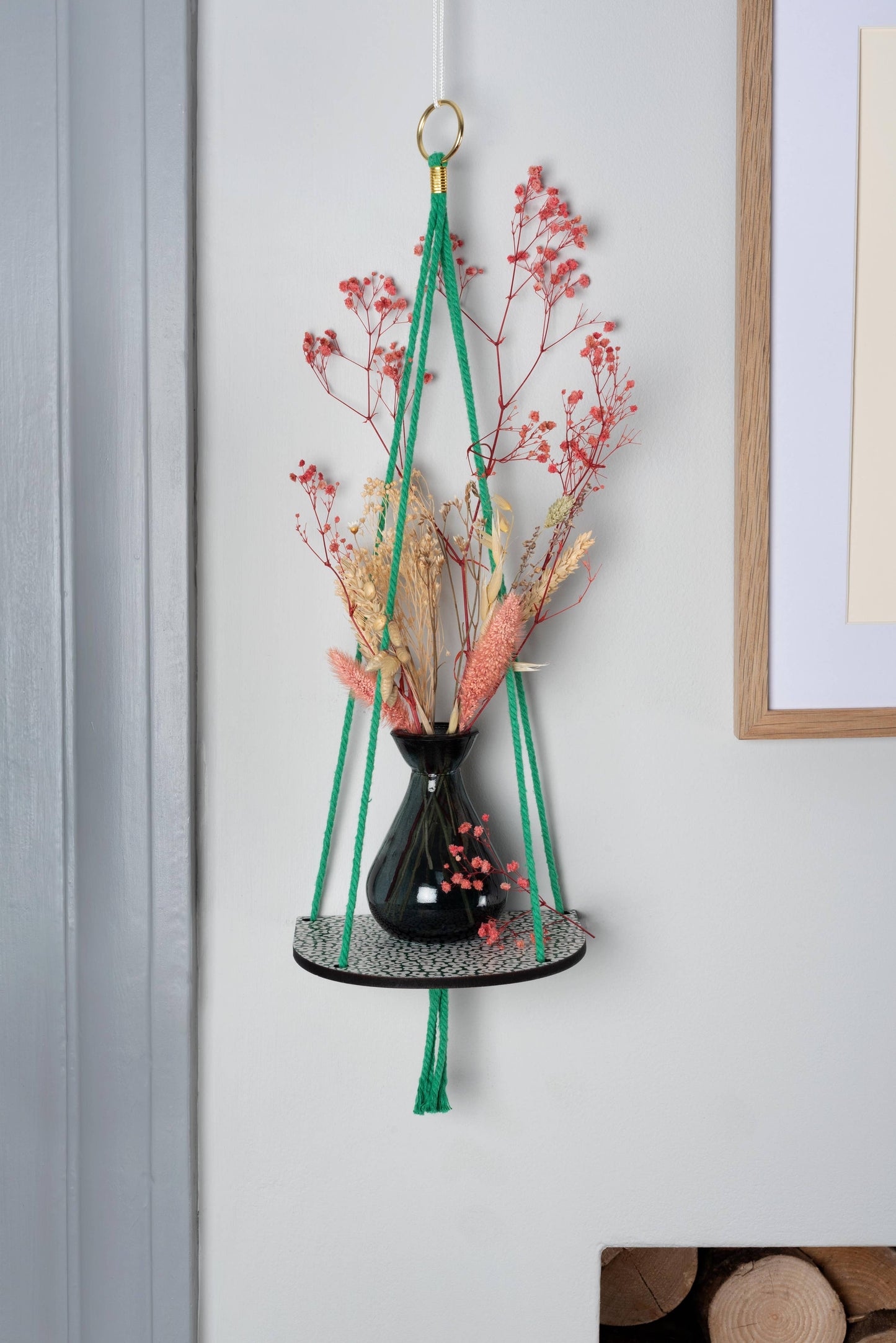 Hanging plant holder with dried flowers against a light gray wall.