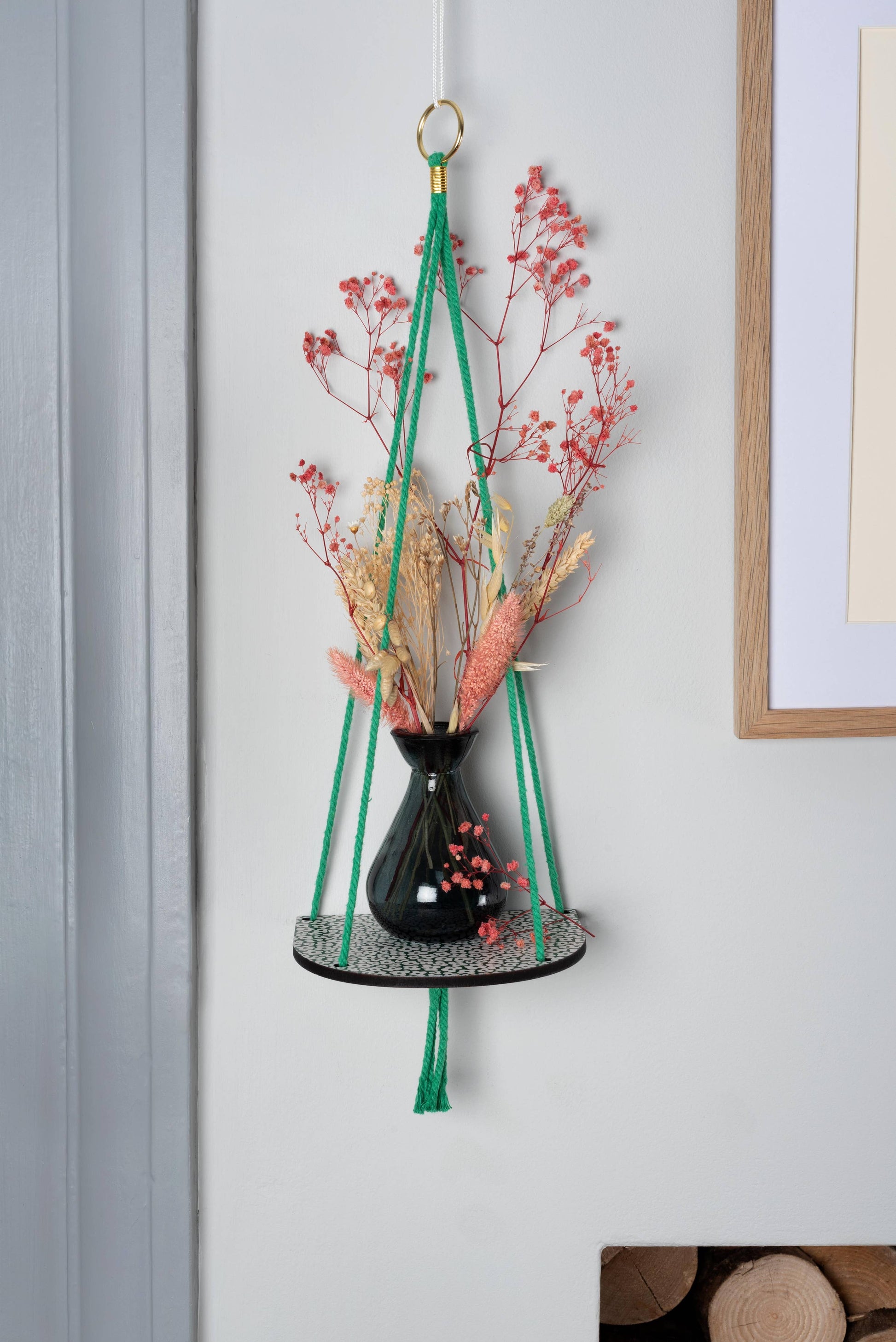 Hanging plant holder with dried flowers against a light gray wall.