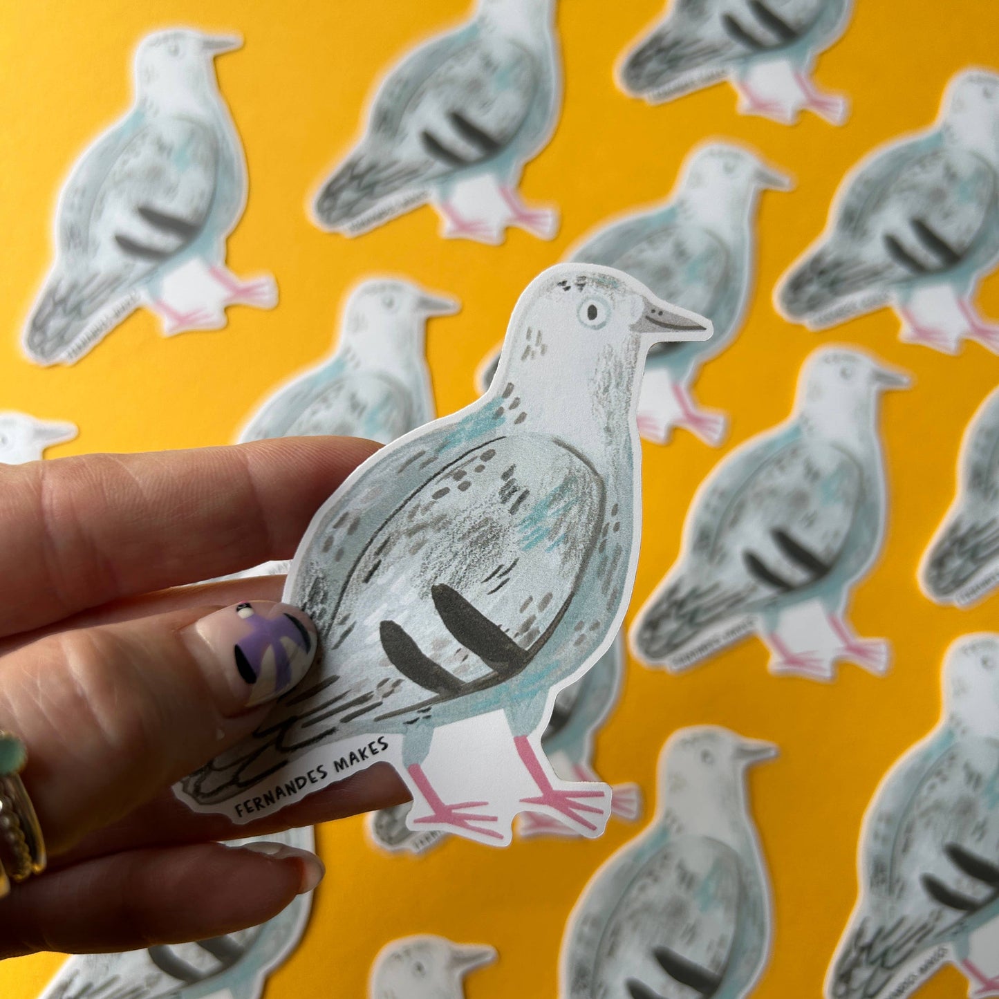 Hand holding a pigeon sticker with more stickers on a yellow background