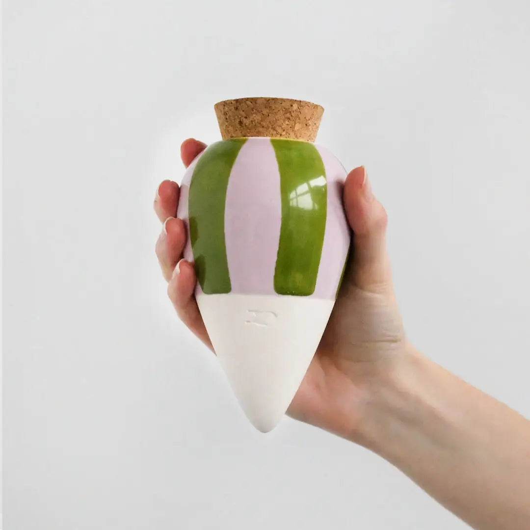 A hand holding a conical ceramic vase with green and lilac stripes on a white background.