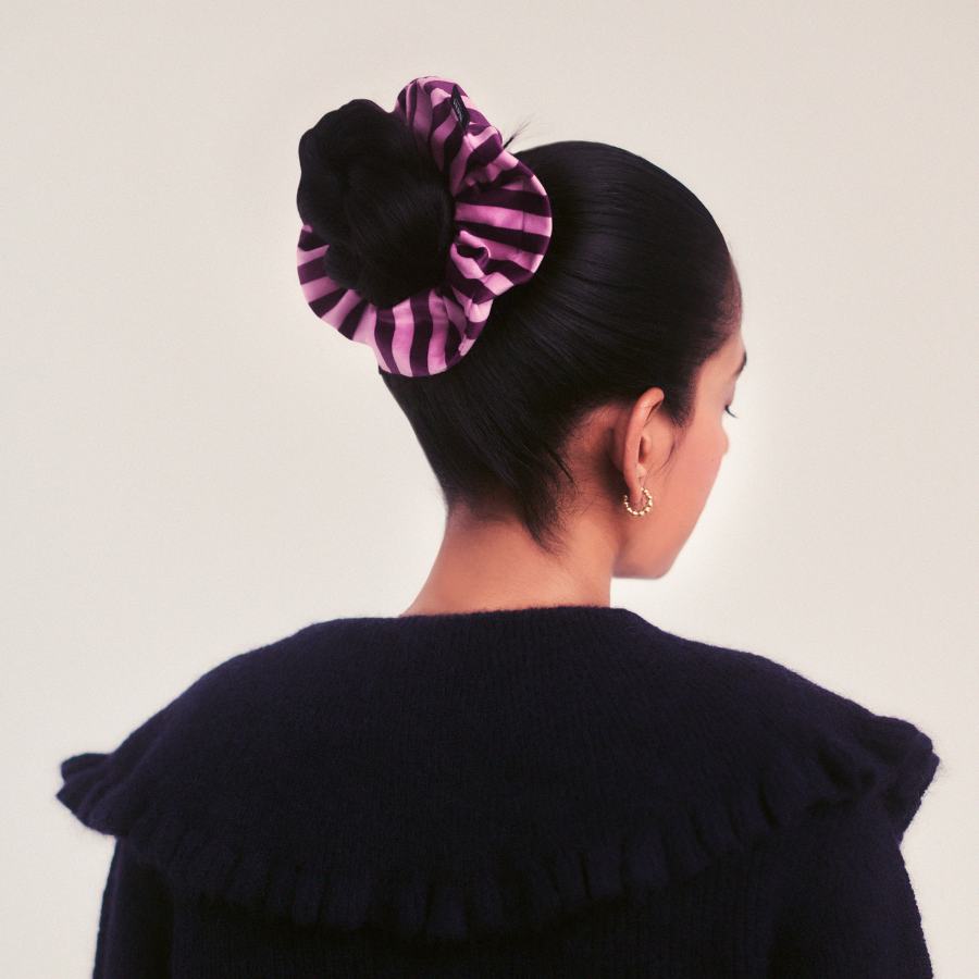 Person wearing a black coat with a pink and black scrunchie in their hair against a white background