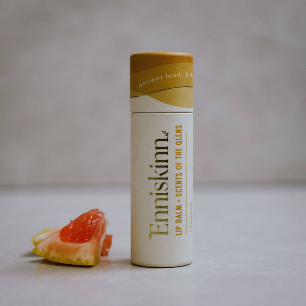 A tube of Enniskinn lip balm with 'Scents of the Glens' written on it, next to a slice of grapefruit.