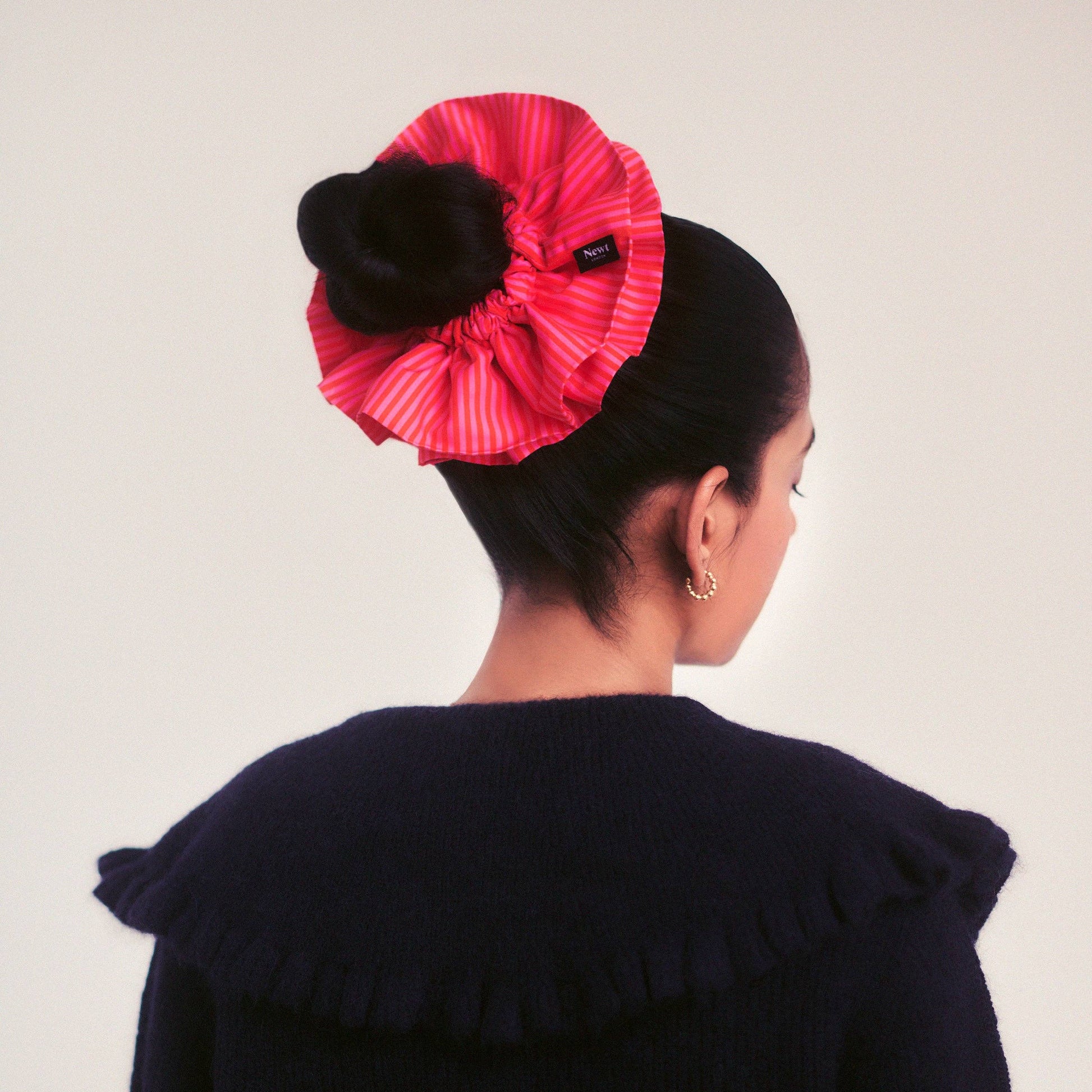 Person wearing a large pink scrunchie with a plain background