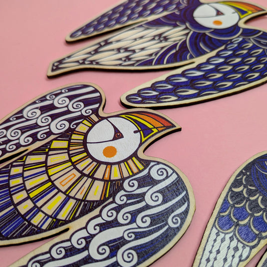 A set of three colorful wooden puffin decorations with intricate patterns in blue and yellow hues, displayed on a pink background.