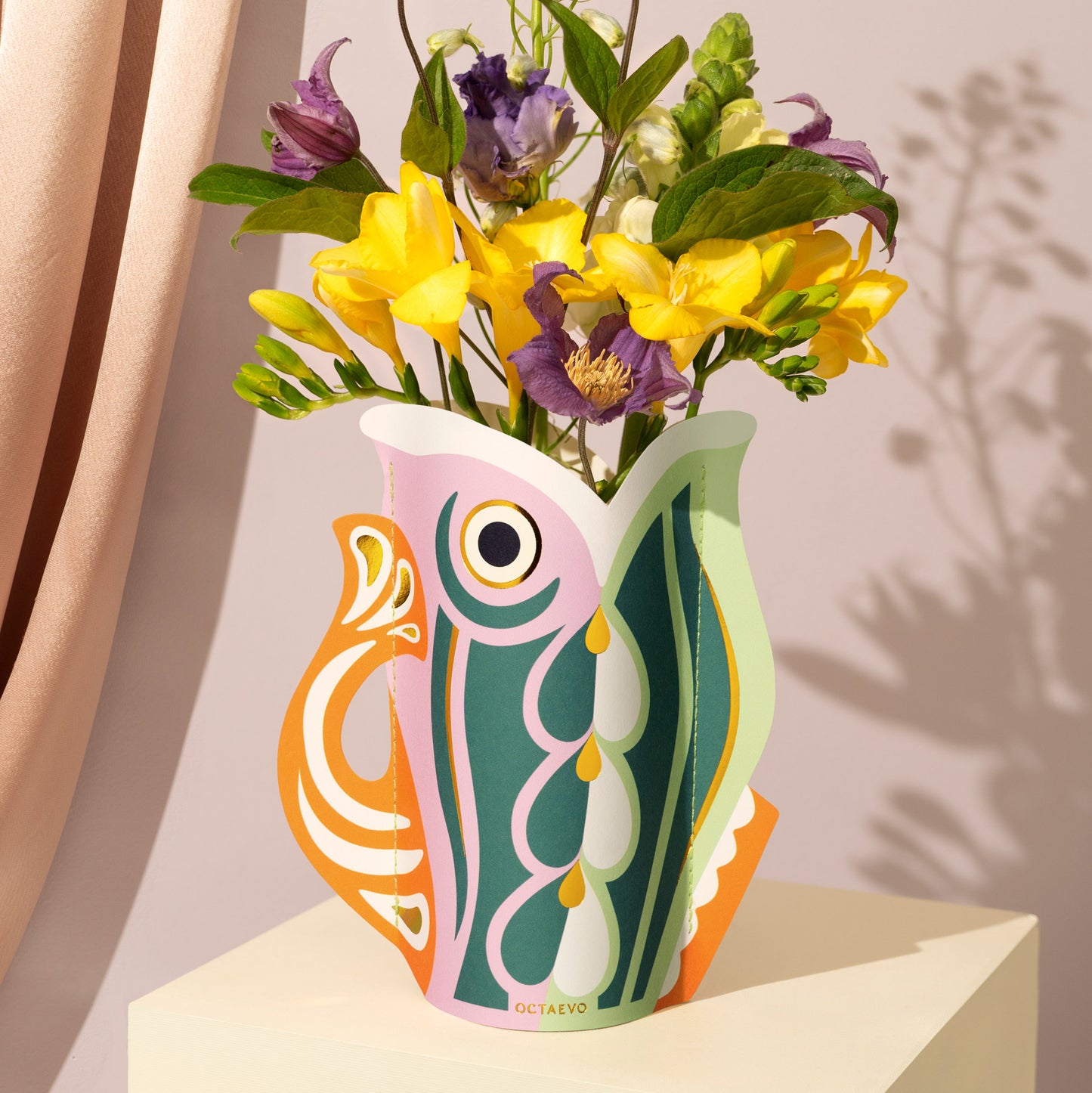 Colorful paper vase with fish design holding flowers on a neutral background