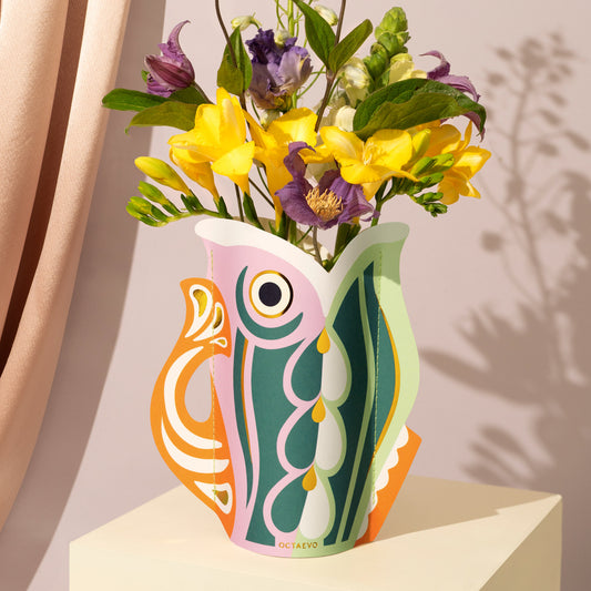 Colorful paper vase with fish design holding flowers on a neutral background