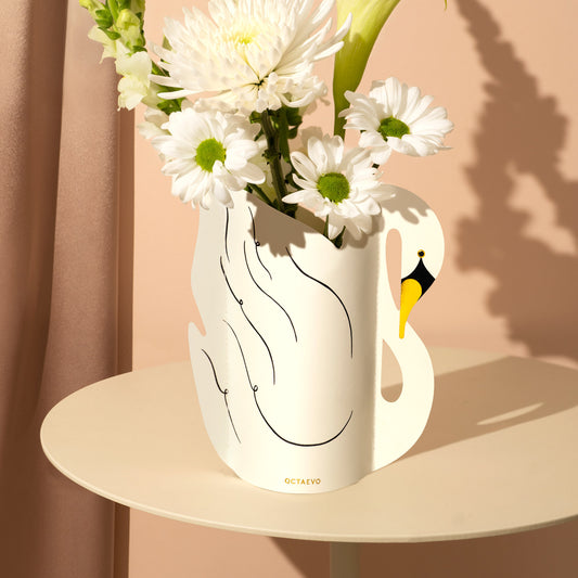 Swan-shaped vase with flowers on a beige surface against a pink background
