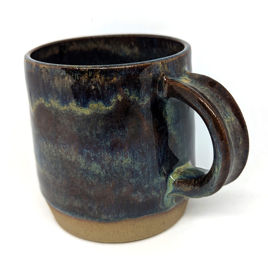A handcrafted ceramic mug with an olive green and blue color palette and a matte finish on the bottom quarter, gloss elsewhere.